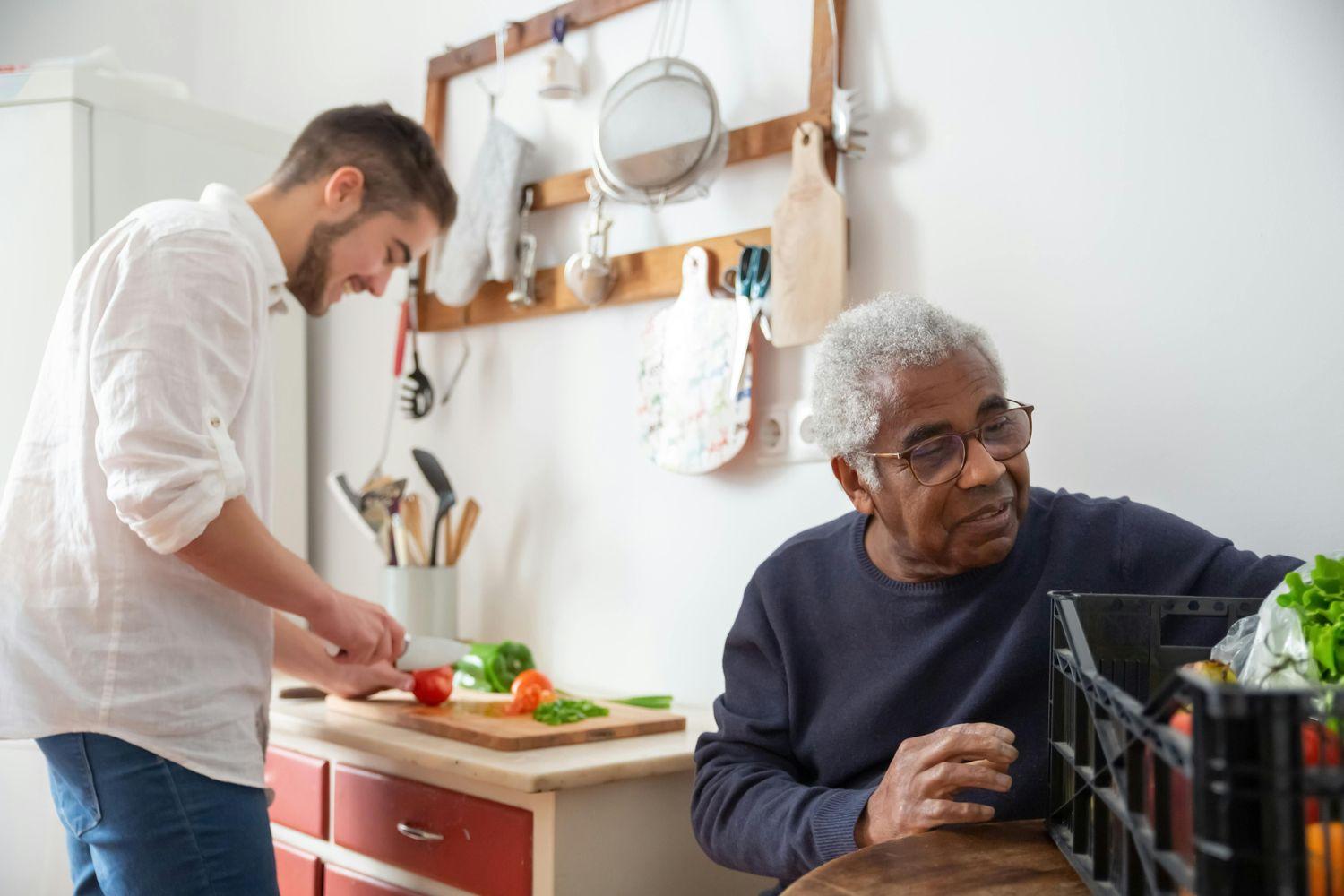 Ein junger Mann kocht mit gesunden Lebensmitteln und ein älterer Mann sitzt