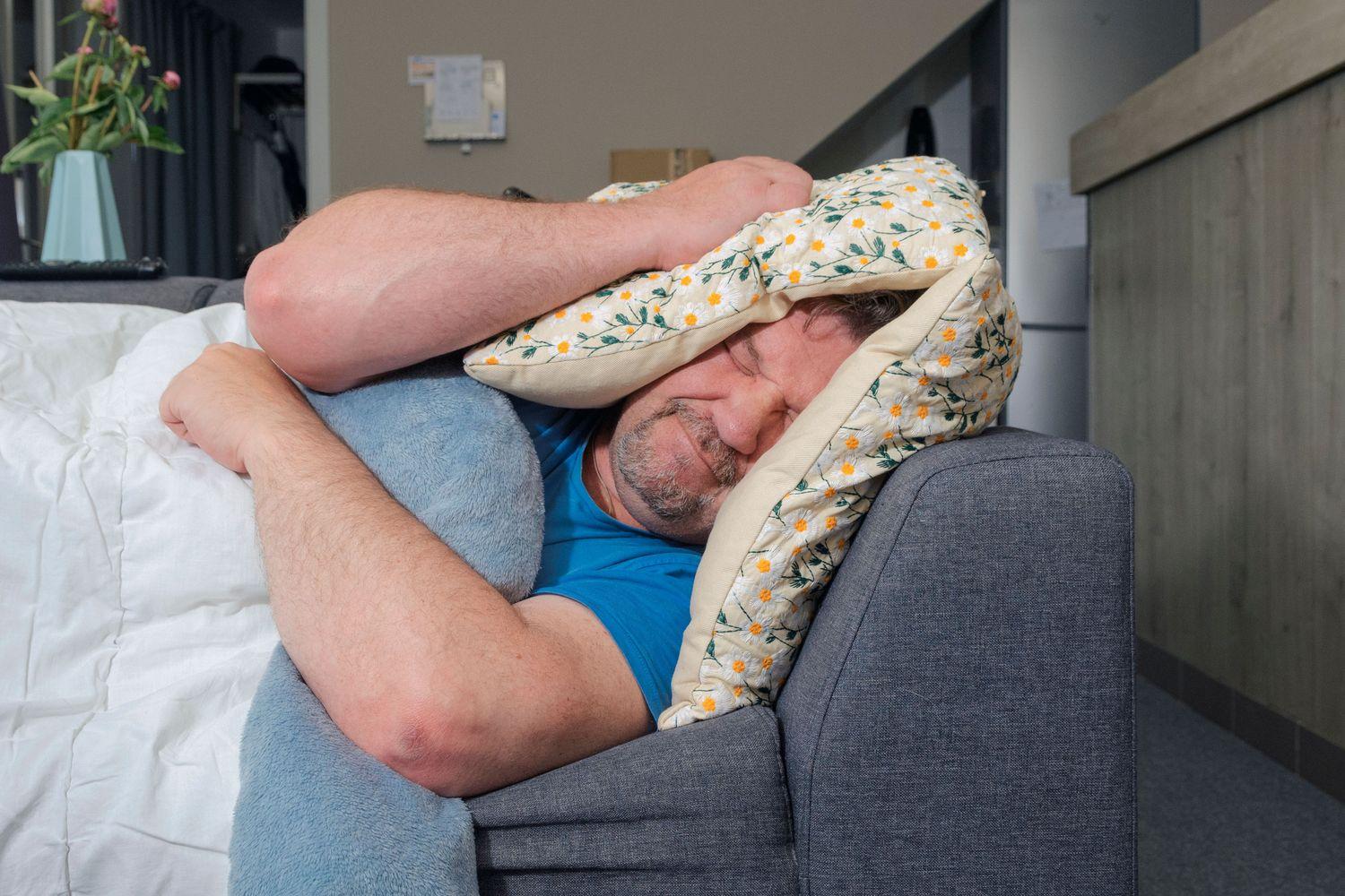 Ein Mann kann wegen Tinnitus nicht schlafen und presst sich ein Polster auf die Ohren