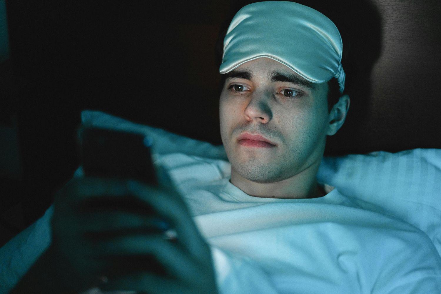 Ein junger Mann liegt im Bett und scrollt auf seinem Smartphone, weil er wegen Tinnitus unter Schlaflosigkeit leidet.