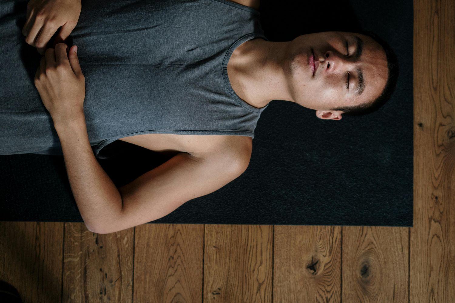 Ein Mann liegt auf einer Yogamatte und macht Entspannungsübungen, um seine Tinnitus-Behandlung zu unterstützen.